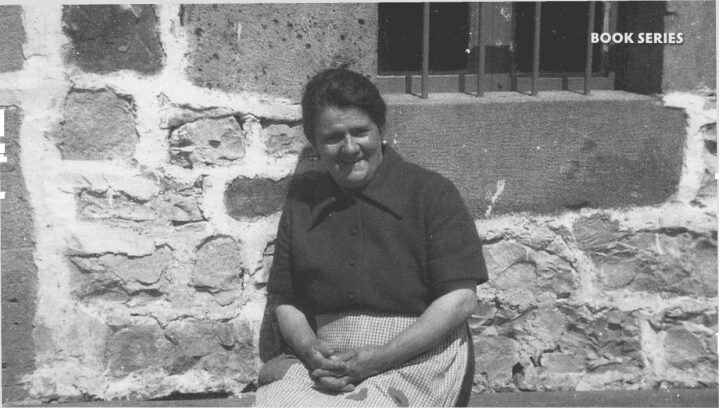 Woman sitting against a stone wall.
