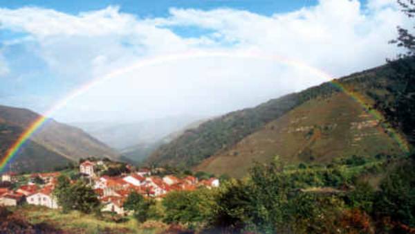 Rainbow arching over village and hills.