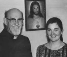 Priest and woman smiling, Jesus portrait behind.