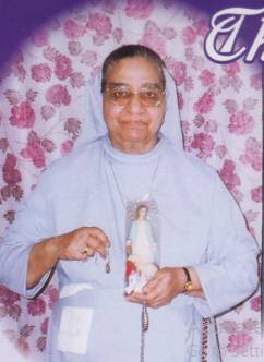 Elderly nun holding religious figurine, smiling.