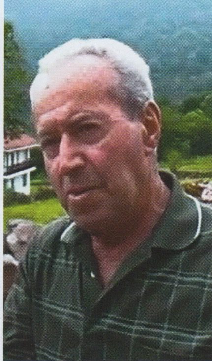Elderly man outdoors with greenery background.