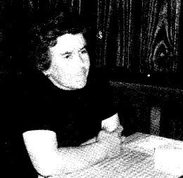 Person sitting at table, dark clothing, thoughtful.