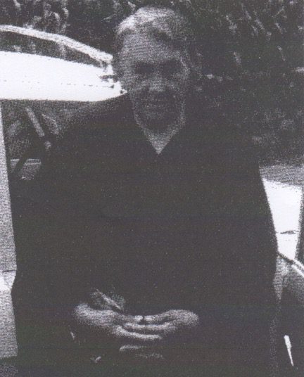 Elderly person seated outdoors in black and white.