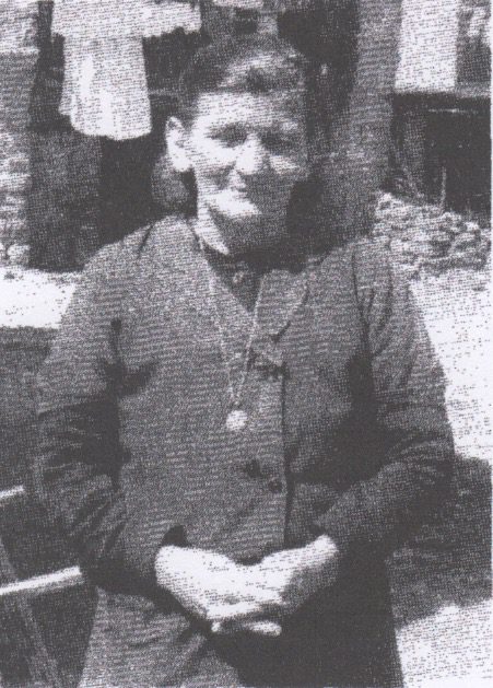 Elderly woman standing outdoors in black attire.