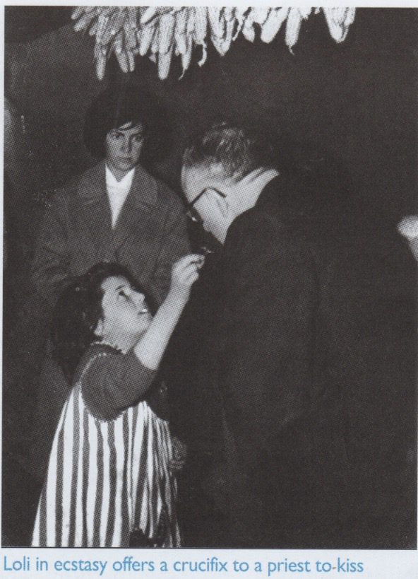 Girl offers crucifix to priest for kiss.