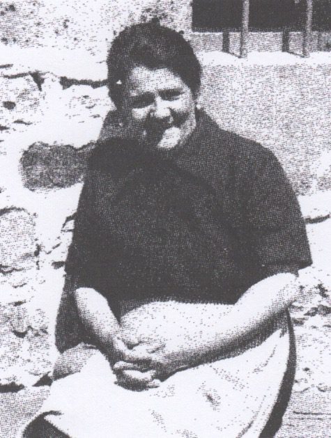 Smiling woman sitting against a stone wall.