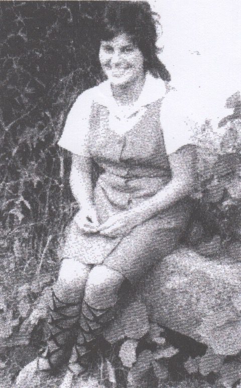Smiling woman sitting on a rock outdoors.